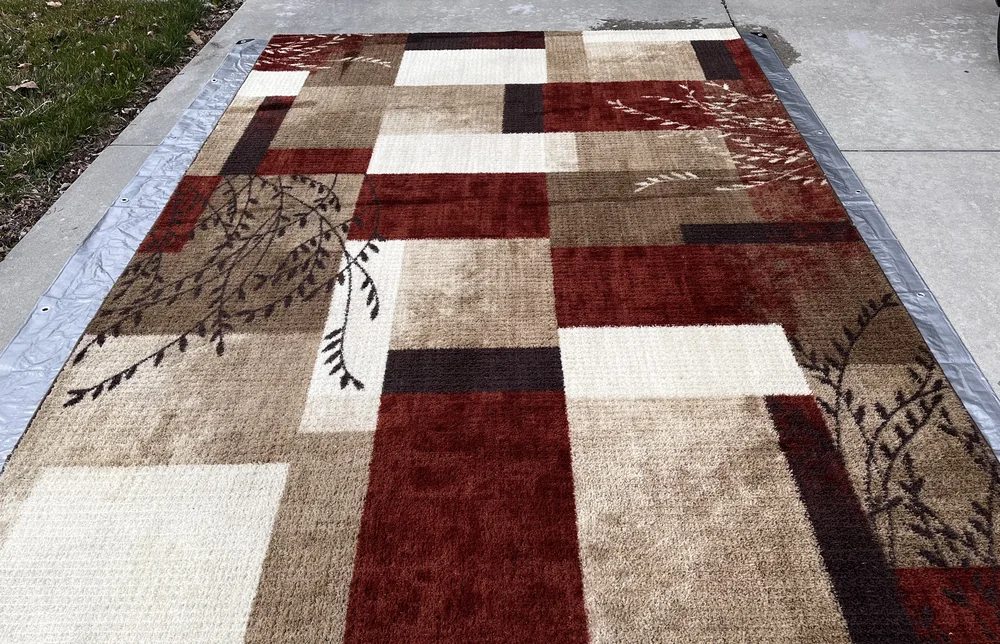 Geometric area rug drying on driveway after deep cleaning